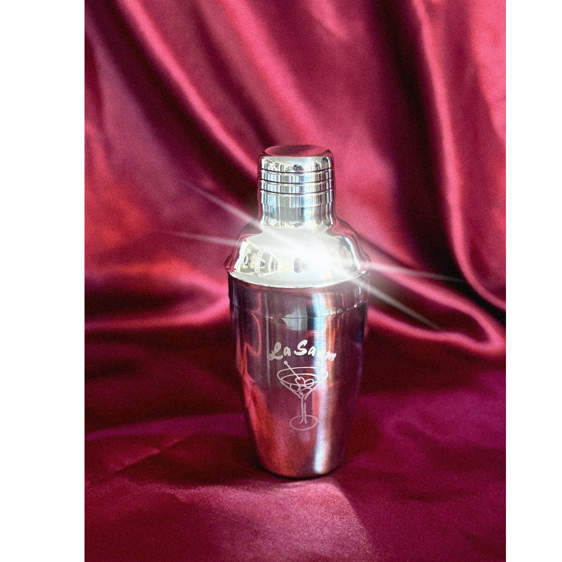 Silver cocktail shaker with 'La Saum' olive brine branding on a red fabric background