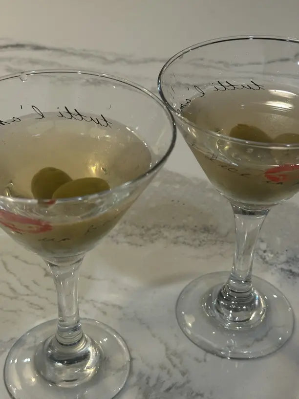 two dirty martinis in glasses on the marble countertop