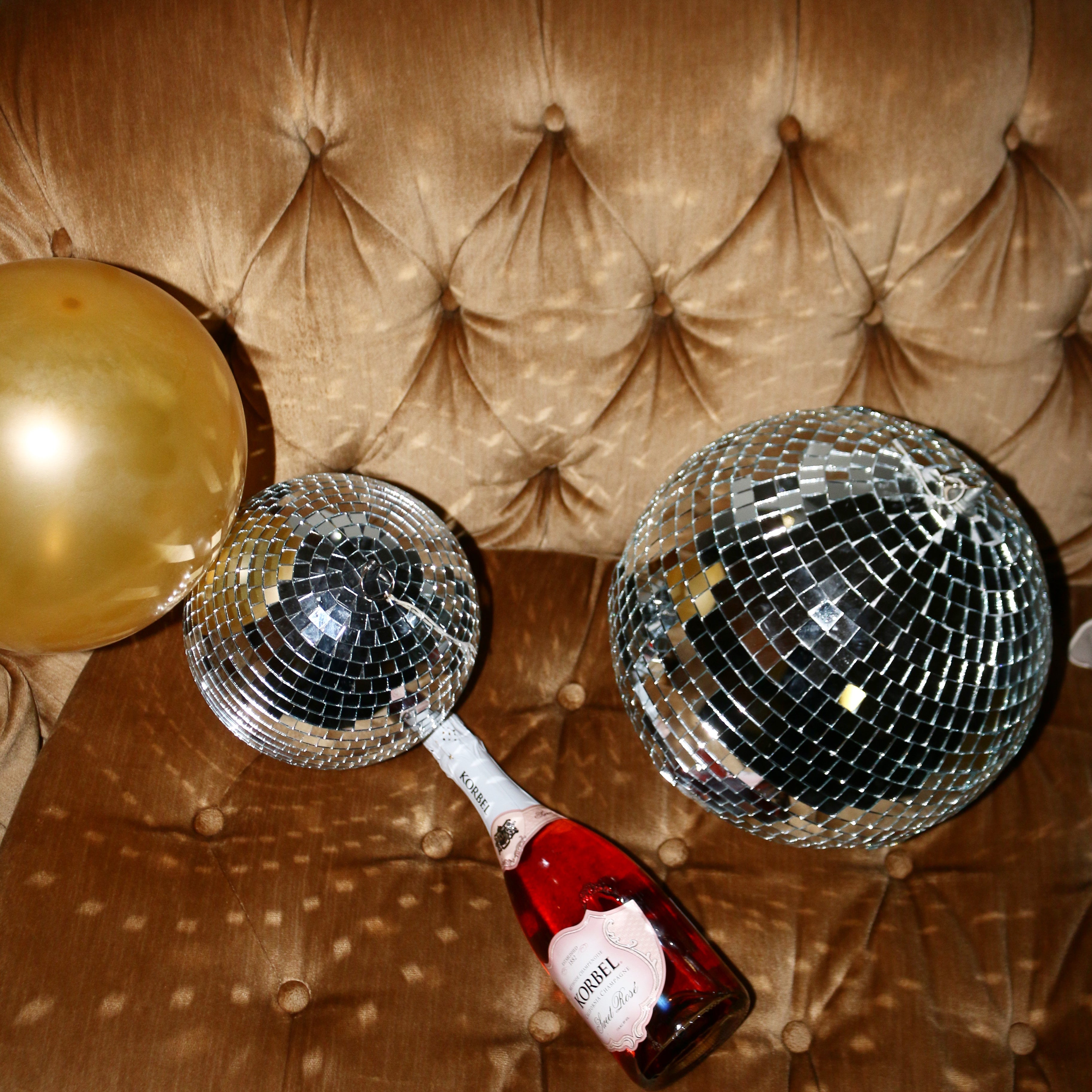 two disco balls on a yellow velvet couch with a bottle of la saum olive brine next to it
