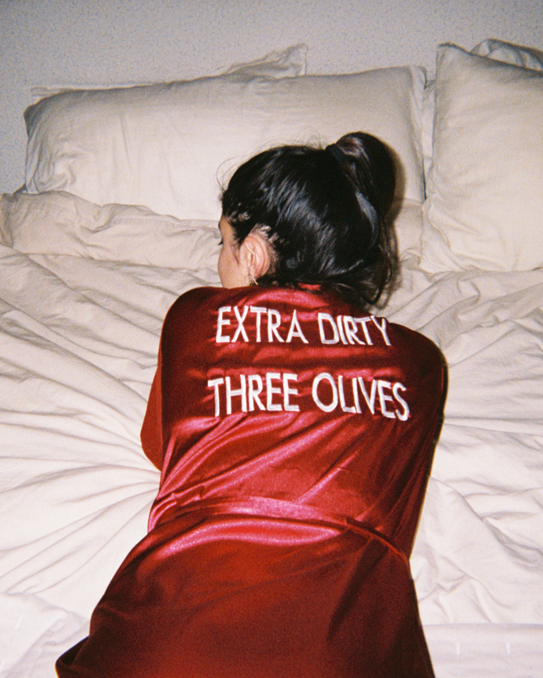 Person wearing a red satin robe with la saum dirty martini  text on it, lying on a bed.