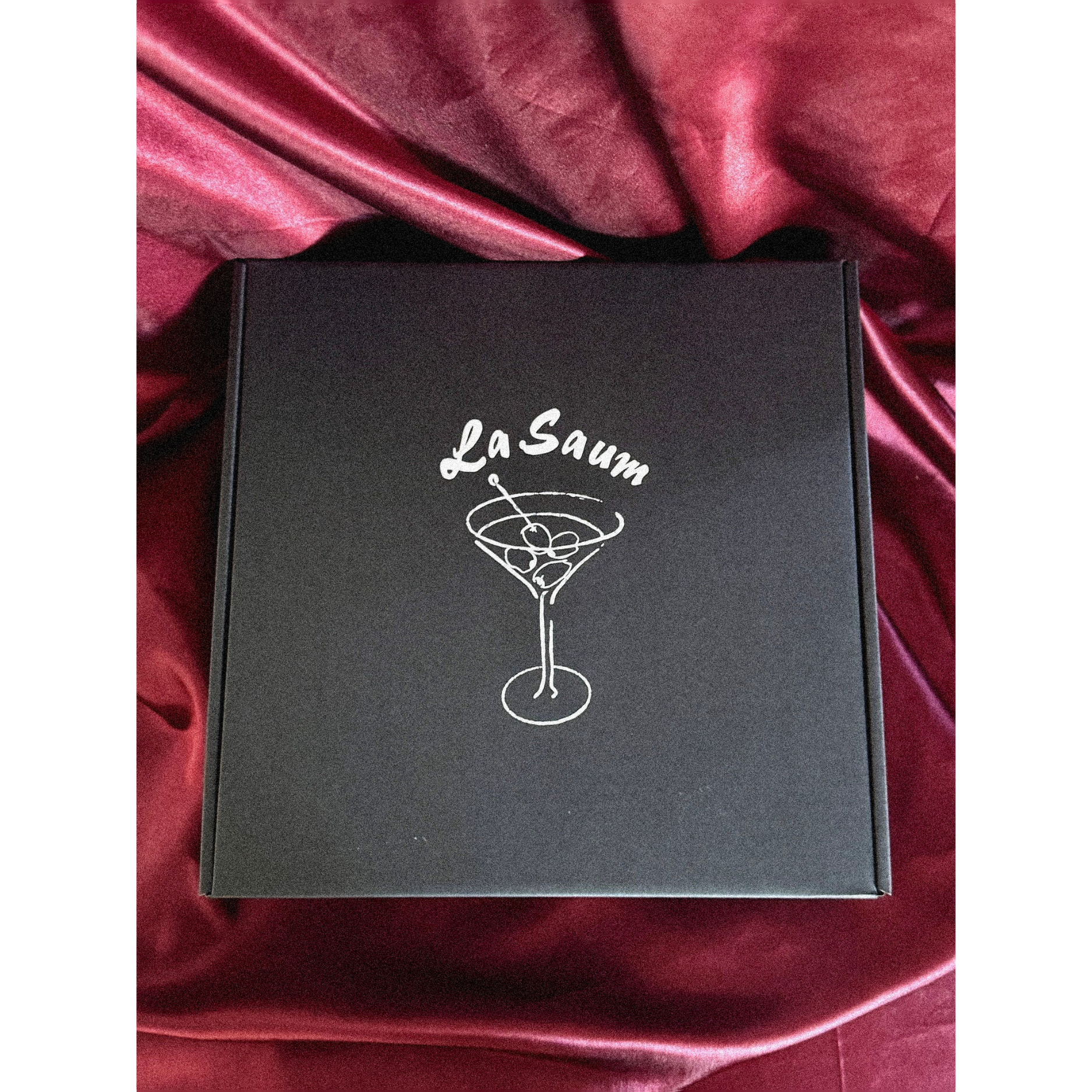 Black box with 'La Saum' olive brine branding on a red satin background